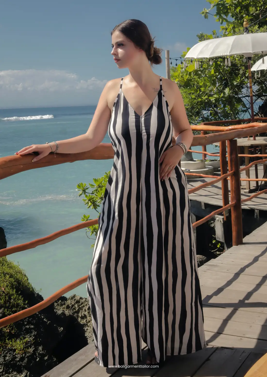 Model in a black and white striped long jumpsuit on a terrace above the sea